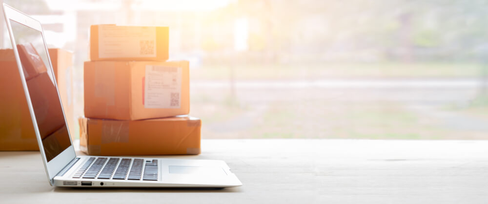 Laptop computer at workplace and cardboard parcel boxes of products to deliver to customers.