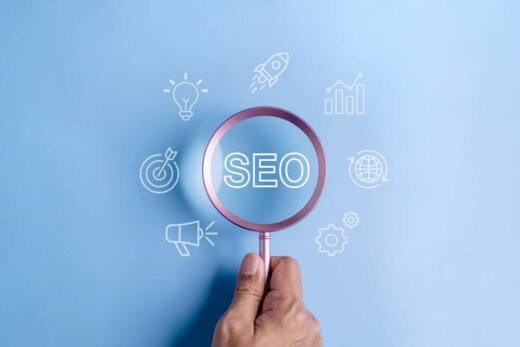 A person holding a magnifying glass above a graphic that spells SEO, along with several others surrounding it.